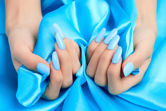 Closeup shot of a female's hands with blue nail polish on a blue silk fabric