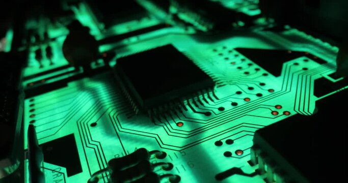 Printed circuit board electronics macro glowing in green light, probe lens between components
