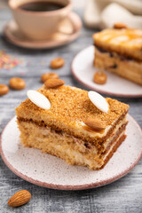 Honey cake with milk cream, caramel, almonds and a cup of coffee on a gray wooden background. Side view, selective focus.