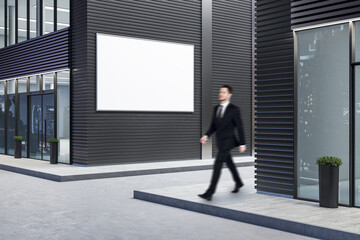 Businessman walking near business center with blank billboard on wall.