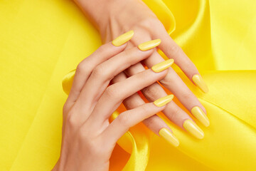 Closeup shot of a female's hands with yellow nail polish on a yellow silk fabric