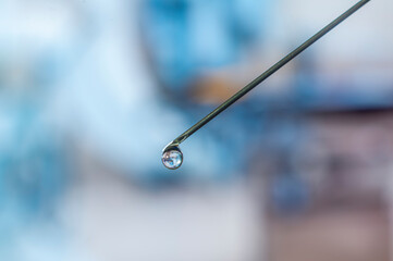 Syringe needle with a drop of serum on top. Blurred background that is reflected in the serum drop.