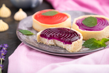 Sweet tartlets with jelly and milk cream with cup of coffee on a black concrete background. Side view, selective focus.