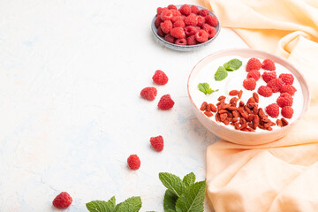 Yogurt with raspberry and goji berries in ceramic bowl on white concrete background. Side view, copy space.