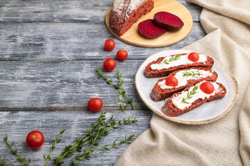 Red beet bread sandwiches with cream cheese and tomatoes on gray wooden background. Side view, copy space.