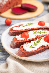 Red beet bread sandwiches with cream cheese and tomatoes on gray wooden background. Side view, selective focus.