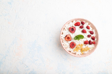 Rice flakes porridge with milk and strawberry in ceramic bowl on white concrete background. Top view, copy space.