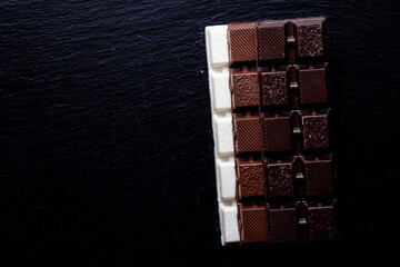 Three types of chocolate - black, milk and white on a black background with copy space