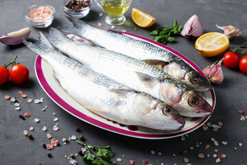 Fresh ready to cook raw mullets with ingredients and seasonings like parsley, lemon, cherry tomatoes, red onion and olive oil on dark background.