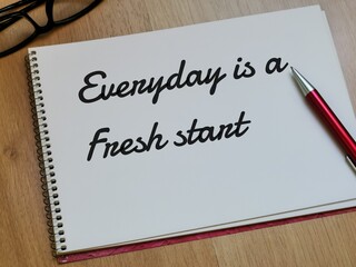 Text Everyday is a fresh start on note book with pen and eye glasses on wooden table.