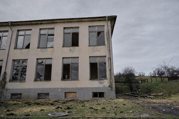 07.01.2021. Bulgaria, Kardzali. Old brownfield and abandoned soviet type school with overcast and very cloudy sky. School inside the green grass with broken windows.
