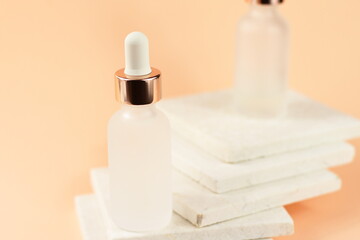 Transparent cosmetic bottles with pipette on natural stone marble background,  organic spa on peach color texture, copy space 