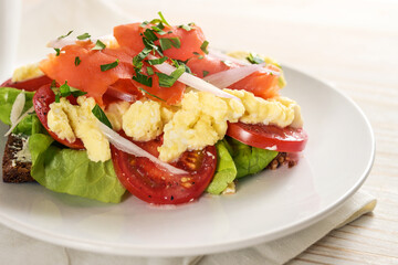 Smoked salmon and scrambled eggs on whole meal bread with tomatoes and lettuce, healthy sandwich meal on a white plate