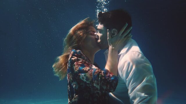 Cinematic shot of young carefree romantic loving couple is kissing with passion in blu underwater during their honey moon vacation holiday. Concept of love, relationship, freedom, sensuality, fantasy.
