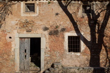 Fototapeta na wymiar An old abandoned mediterranean style country house with a dead tree in the mountains at the beautiful island of Mallorca located at the Sierra de Tramuntana on a sunny clear day at the golden hour