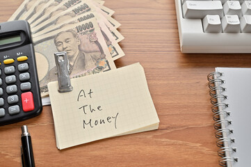 On the desk were Japanese yen bills, a keyboard, a notebook, and a word book with the word at the money .