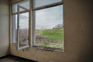 Old type window made of wood with scene of small hill covered by green grass and trees under overcast and cloudy sky background in Bulgaria.