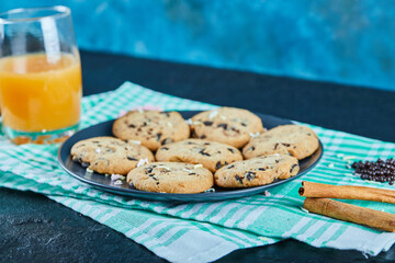 A plate of chocolate chips cookies and a glass of orange juice on dark table with cinnamon
