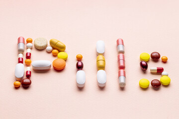word pills made by assorted pill, tablets and capsules isolated on pink background. pharmacy industry concept. above view