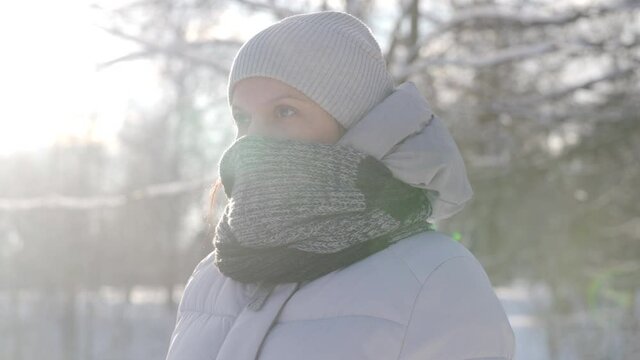 Portrait of adult woman in winter park on cold sunny day, face of woman wearing a hat and scarf closeup