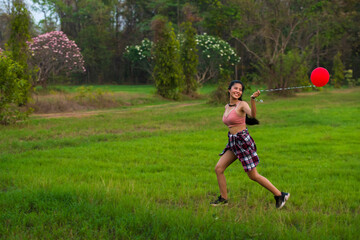 Fototapeta premium A beautiful woman with red balloons is playing in the green lawn.