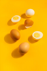 Brown chicken raw and hard boiled fresh eggs on yellow background. Healthy food or Happy Easter concept. Top view, flat lay