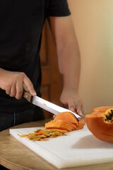 man cutting fresh papaya on a chopping board, on a wooden table. The concept of healthy eating.