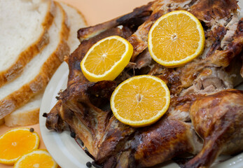 Whole roasted chicken or duck on white plate, decorated with fresh oranges and bread. Selective focus.