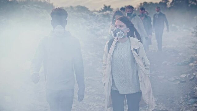 Group of Young Volunteers in Gas Masks Take Care of the Environment While Going Through the Toxic Smoke at Garbage Dump.Worldwide Global Problem of Pollution of Planet.Responsibility by the Future