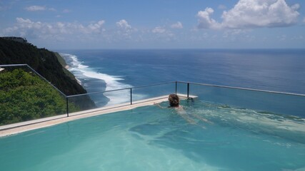 Luxurious resorts concept. Young woman swimming in an infinity pool with the breathtaking view of an ocean