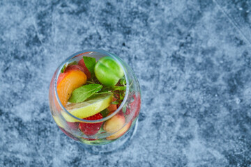 A glass of juice with whole fruits inside on blue background