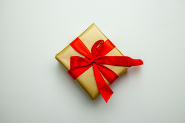 A holiday gift. Box in a gold gift wrapping with a red bow, on a white background. Merry Christmas, Happy New Year and Valentine's Day greetings. Postcard. High quality photo