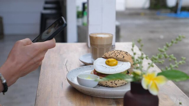 Hand taking pictures of healthy delicious cruelty free vegan lunch of a burger and cappuccino with a smartphone. 