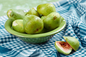 A bowl of juicy green figs and slices of fig on a blue tablecloth