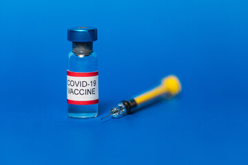 Vial filled with Covid-19 vaccine and syringe on blue background.