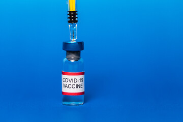 Vial filled with Covid-19 vaccine with punctured syringe on blue background