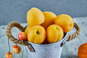 Delicious ripe apricots in iron bucket with cherries on marble background