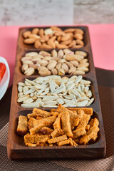 Assorted snacks on the pink table. Pistachios, sunflower seeds, almonds, crackers