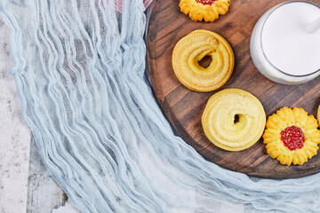 Assorted biscuits and a jar of milk on a wooden plate with tablecloths