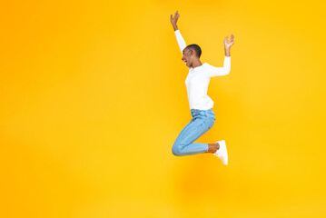 Happy excited African American woman jumping with hands raising in yellow isolated studio background with copy space