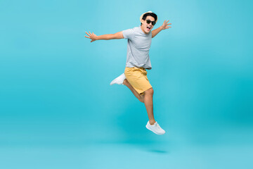 Fototapeta na wymiar Happy handsome Asian tourist man in casual attire jumping studio shot isolated on light blue background