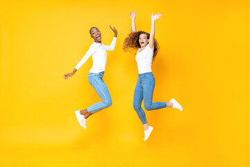 Two interracial woman friends jumping freely in isolated studio yellow color background