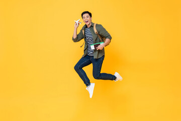 Fototapeta na wymiar Young handsome Asian tourist man holding airplane model, passport and boarding pass jumping in isolated yellow color background