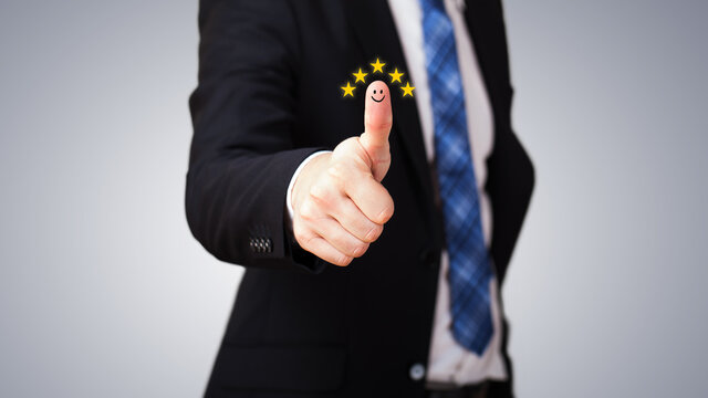 businessman showing a thumbs up gesture with a smile emoticon and 5 stars in front of grey background