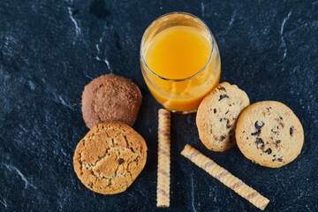 A glass of orange juice and group of various cookies on dark background