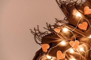 Paper hearts and a glowing garland sit on a brown fringed scarf. Composition for Valentine's Day....