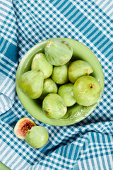 A bowl of juicy green figs and slices of fig on a blue tablecloth