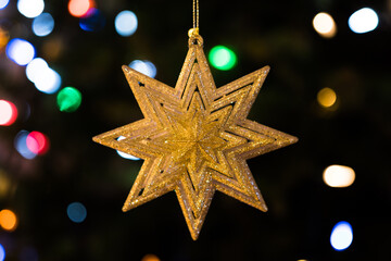 Hanging star Christmas tree ornament and blurred lights background. Seasons greetings holiday card theme