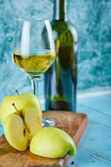 A glass of white wine and bottle with apple slices on blue background