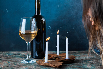 Woman blowing out candles with a glass of white wine and bottle on marble table